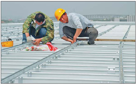 Workers lay solar panels on a roof at Nanjing South Railway Station. China is giving attention to reducing energy consumption in industrial production. [China Daily]